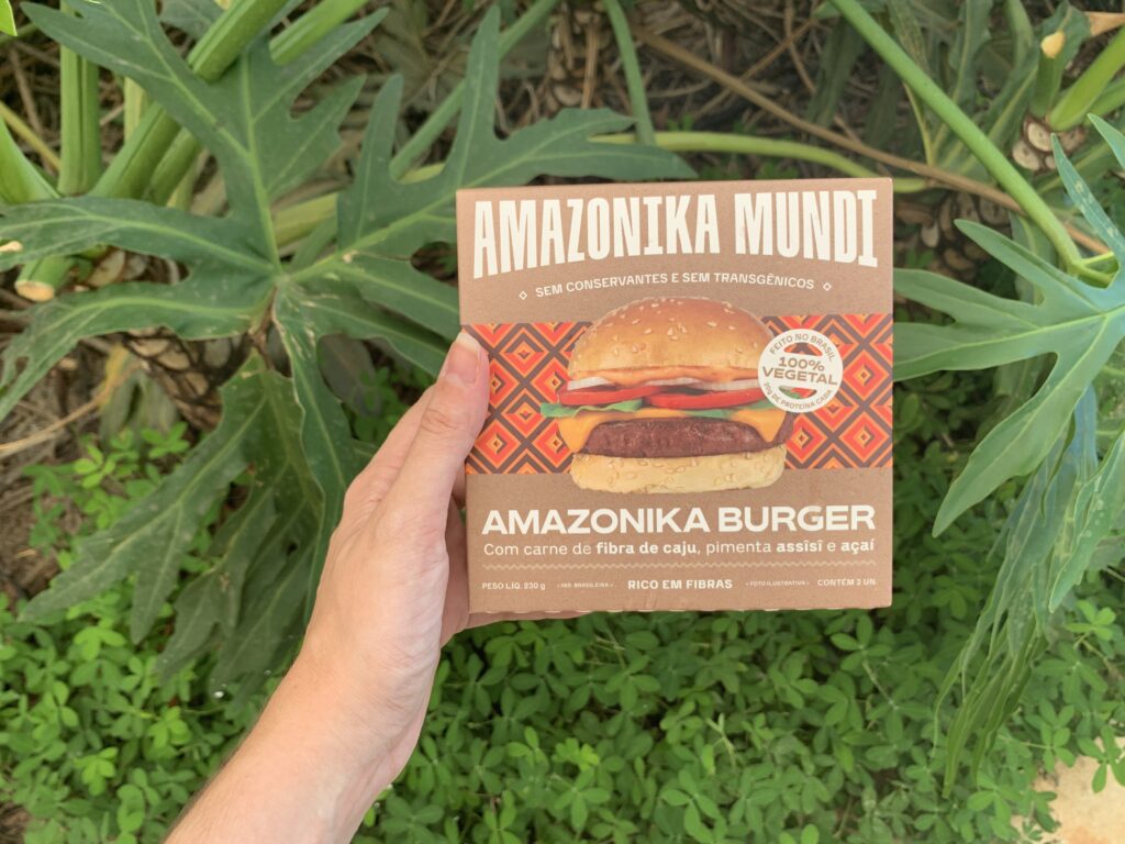 Mão segura caixinha de Amazonika Burger num fundo verde